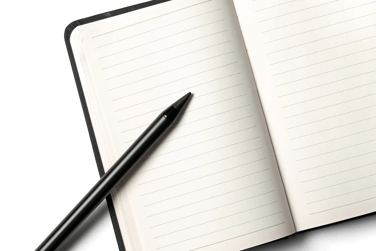 A black pen resting across an open lined notebook.