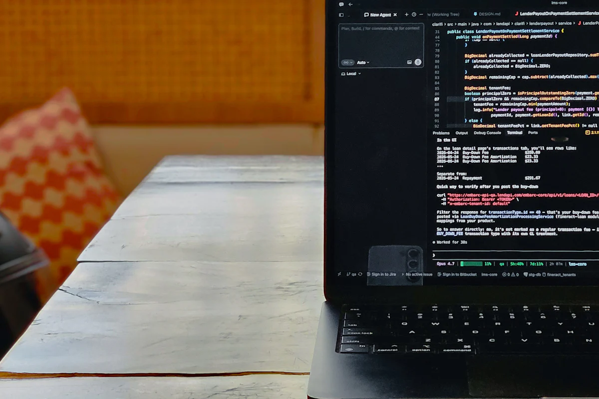A laptop displaying programming code and an agent interface on a wooden table.