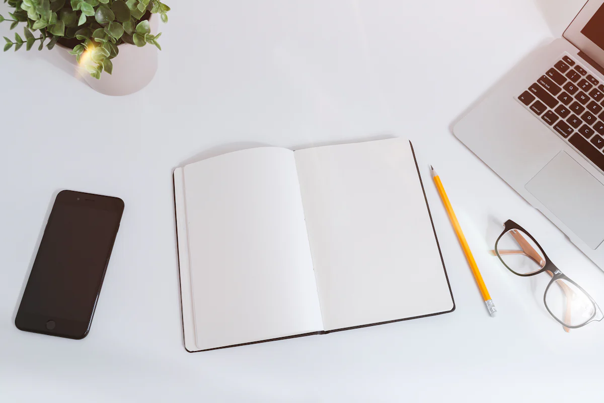 An open notebook, phone, and laptop on a clean white desk.