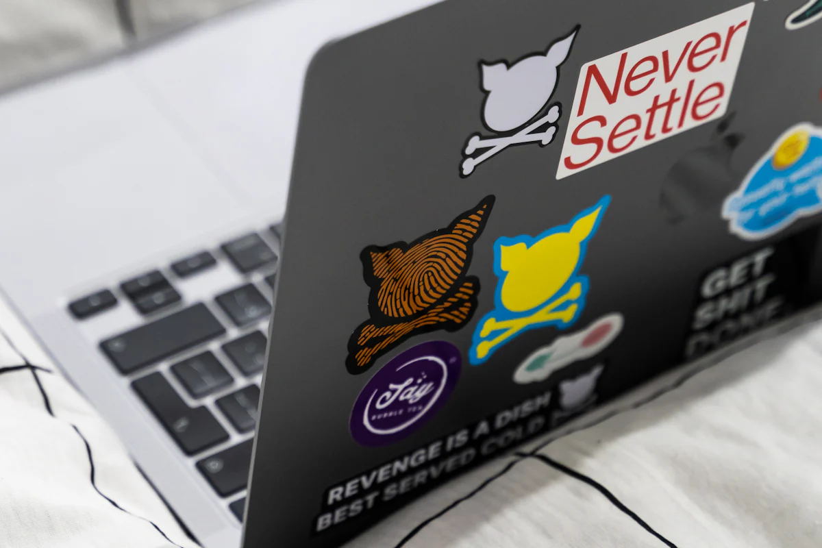A laptop with stickers on its case resting on a bed.